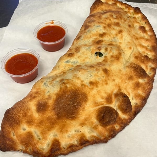 Golden-brown calzone with two small cups of red marinara sauce on white parchment paper.