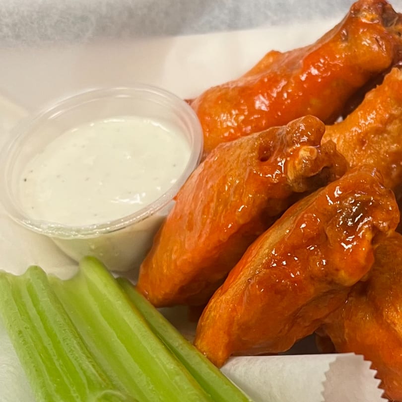 Close-up of buffalo wings with ranch dressing and celery sticks in a white container.