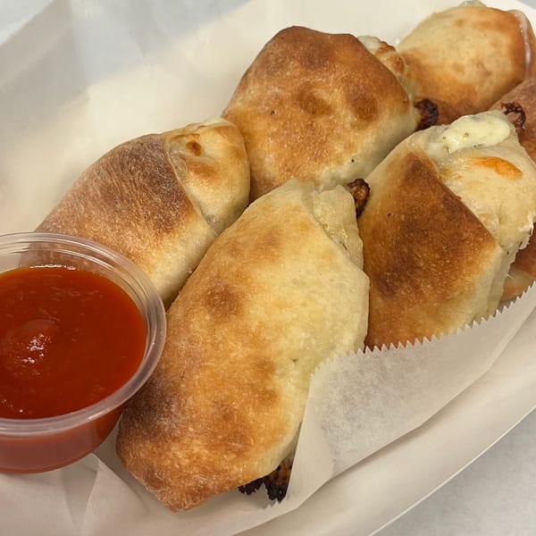 Golden-brown Capo's Pizzeria garlic knots with melted cheese, served in a white paper tray with marinara sauce.