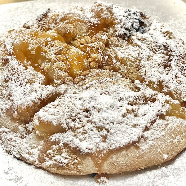 Close-up of a dessert pizza with apple filling, streusel topping, and powdered sugar.