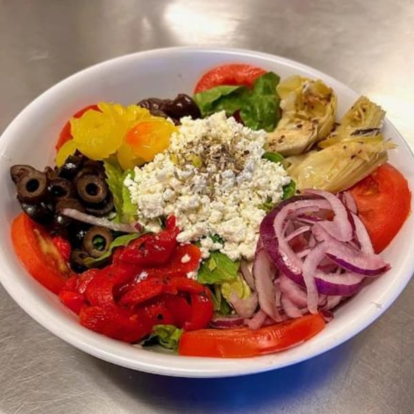 A vibrant salad with feta, olives, artichokes, roasted peppers, onions, and tomatoes in a white bowl.