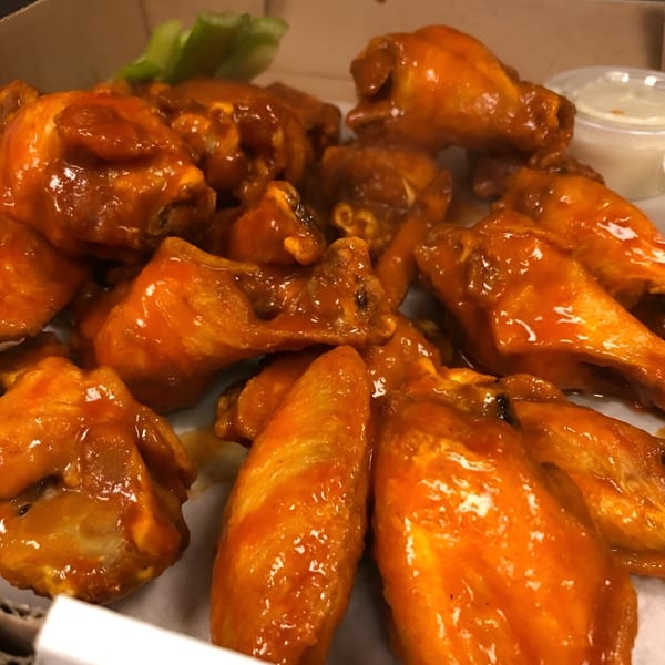 Close-up of Capo's Pizzeria's buffalo wings, coated in shiny orange sauce, with celery and dip.